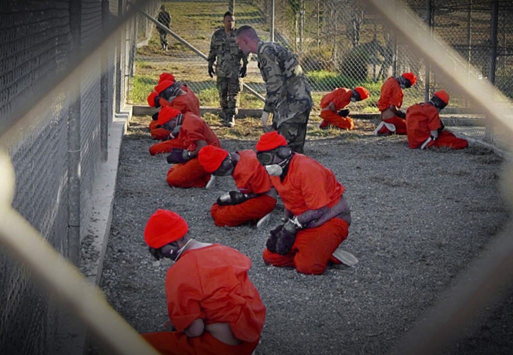ap foto : ap : ** file ** in this jan. 11, 2002 file photo, released by the department of defense, detainees wearing orange jump suits sit in a holding area as military police patrol during in-processing at the temporary detention facility camp x-ray on guantanamo bay u.s. naval base in cuba. (ap photo/u.s. navy, shane t.mccoy, file) a jan. 11, 2002 file photo - released by the department of defense ap provides access to this publicly distributed handout photo to be used only to illustrate news reporting or commentary on the facts or events depicted in this image guantanamo politic automatarkiverad